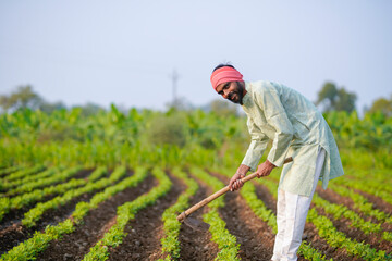 young indian farmer holding farming tool standing at field