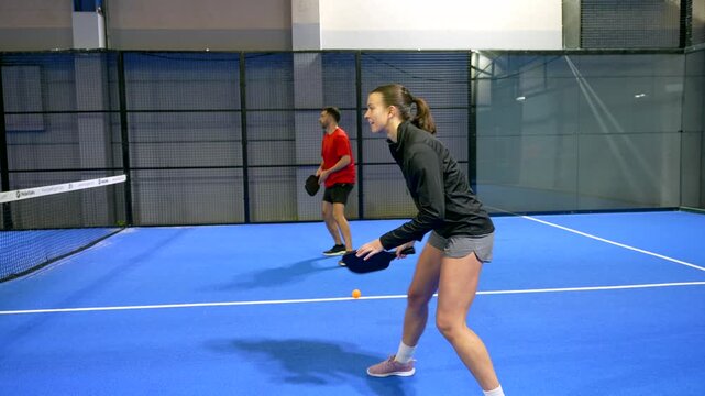 Focused female athlete hitting a dink shot over the net during a friendly doubles pickleball match with her partner on a bright blue court, showcasing a fun and active lifestyle