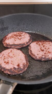 Three hamburgers are cooking in a pan on a stove. The hamburgers are brown and appear to be well-done