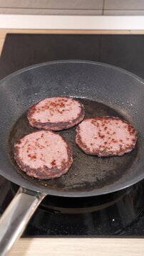 Three hamburgers are cooking in a pan on a stove. The pan is black and the hamburgers are brown