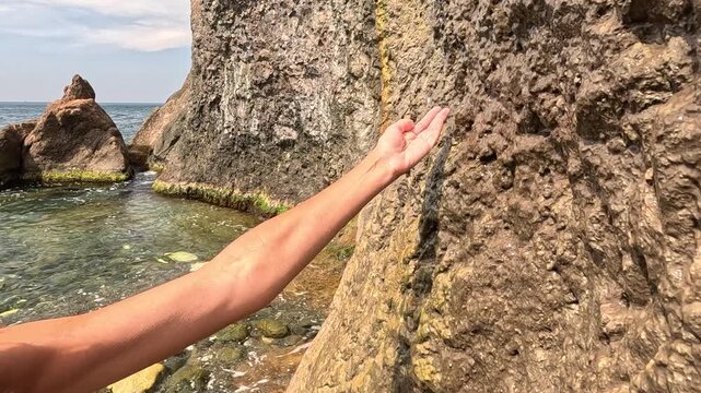 Water cliff hand woman catches refreshing dripping water from natural rock by the sea