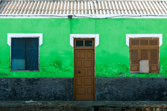 Piccolo edificio con parete verde brillante, porta centrale e finestre con persiane consumate. Colori vivaci e segni di usura ideali per temi di architettura, urbanit&agrave; e autenticit&agrave; visiva.