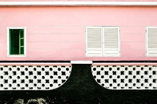 Parete rosa con finestra aperta e persiane bianche sopra pannelli decorativi bianchi e neri. Contrasto tra colori pastello e motivi geometrici, ideale per temi di architettura e design.