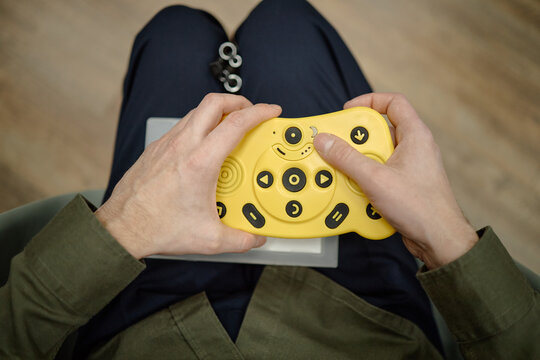 Blind man using tactile braille electronic device with large yellow buttons while sitting in library, hands holding assistive technology for visually impaired