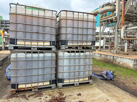 Stack of intermediate bulk containers (IBCs) filled with dark industrial liquid, possibly oil or chemicals, stored on pallets at an outdoor processing facility