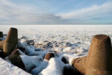 Concrete tetrapods breakwater covered in snow and ice on the seashore in winter. Frozen sea with pancake ice floes under a cloudy sky. Coastal protection, arctic climate and cold weather concept. © Igor