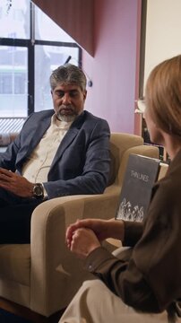 Vertical low angle shot of confident biracial man discussing new book while giving interview in bookstore