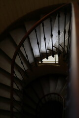 Fototapeta premium Top down view of a vintage wooden spiral staircase with a window. High-angle shot of a classic wooden spiral staircase in an old house. The composition features elegant curves, wrought iron railings, 