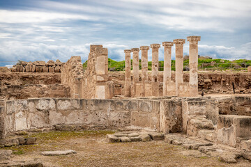 Fototapeta premium Archaeological Site of Paphos UNESCO ruins with stone columns and excavated walls under dramatic sky, Cyprus. Ancient remains in Nea Paphos archaeological park landscape.
