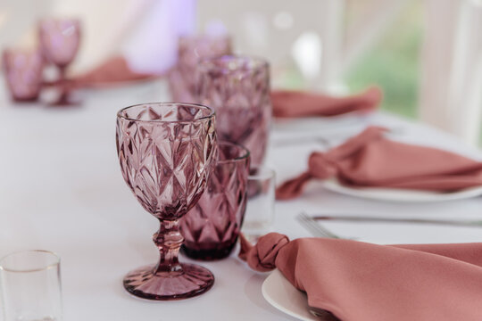 Elegant table setting with pink glasses and napkins. The arrangement features crystal-like goblets and neatly folded cloth napkins on a white tablecloth.