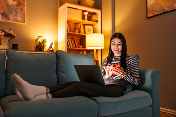 Obraz premium Woman working from home late at night using laptop computer and smart phone