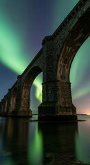 Fototapeta premium Low angle of stone bridge with arches in water reflecting aurora borealis lights against starry sky, representing travel, engineering and nature