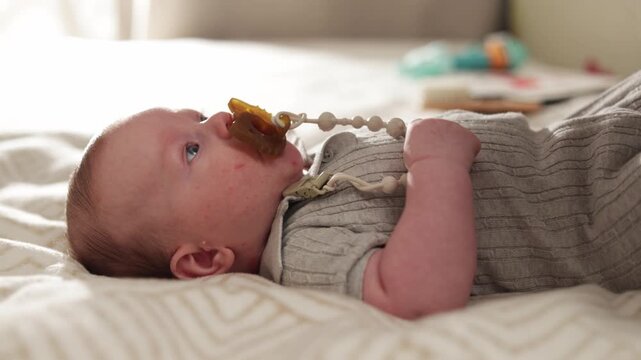 Close-up of a baby lying down with a pacifier in its mouth and a beaded clip attached