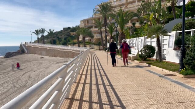 Caminando con bastones de senderismo y trekking ortop&eacute;dicos en marcha por paseo mar&iacute;timo junto a la playa