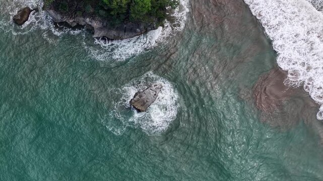 Aerial View of Rocky Tropical Coastline With Crashing Waves and Lush Green Forest