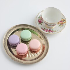 Assorted macarons on a silver platter with a floral teacup nearby.