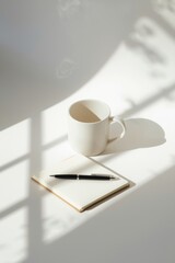 A white coffee cup sits next to a notepad and pen on a white surface.