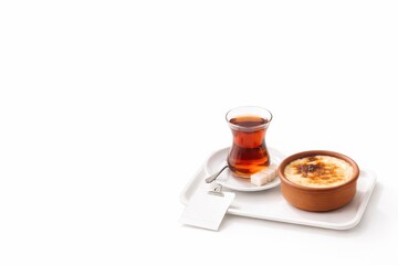 Traditional turkish tea in tulip glass with sutlac rice pudding in clay bowl caramelized top and cinnamon on white tray © Artcuboy