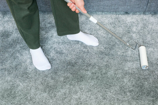 A woman removes dirt from a carpet using mop with a lint roller.