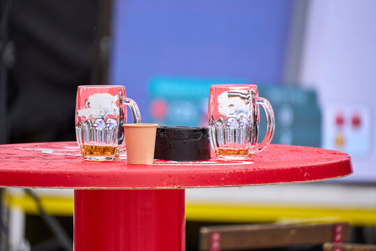 Wet table with empty beer mugs, paper cup, and ashtray, signifying a finished social gathering