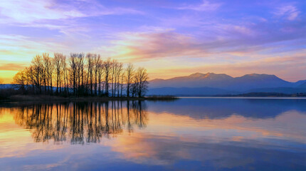 Obraz premium A serene lake at sunset with trees and mountains in the background