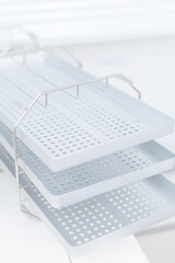 Stacked perforated dental instrument trays on metal rack for sterilization storage and organized clinic preparation
