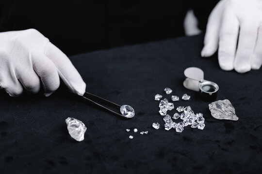 Jeweler handling diamonds with tools and gloves on black surface, workshop mining factory