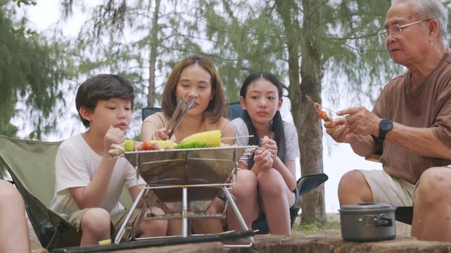 Family enjoy camp summer food, happy moments for children and senior cooking picnic meals together during outdoor travel vacation, creating cherished memories on sunny day.