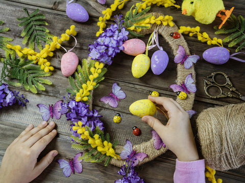 Child's hands decorating an Easter wreath with eggs and spring flowers