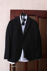 Black tuxedo with bow tie and white shirt hanging on a door before the wedding.