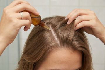 Fototapeta premium Woman applying nourishing scalp oil along hair parting at home, close up, concept of post winter hair and scalp care.