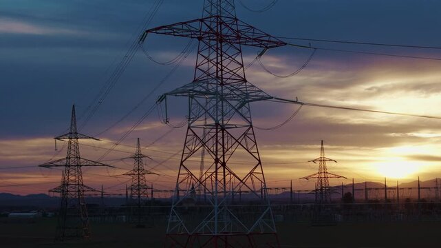High-voltage electrical substation switchyard shows transformers and transmission lines during dramatic sunset sky in a rural area.