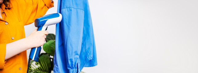 Woman steaming blue shirt with handheld garment steamer. Professional clothing care and laundry service concept. © 5ph