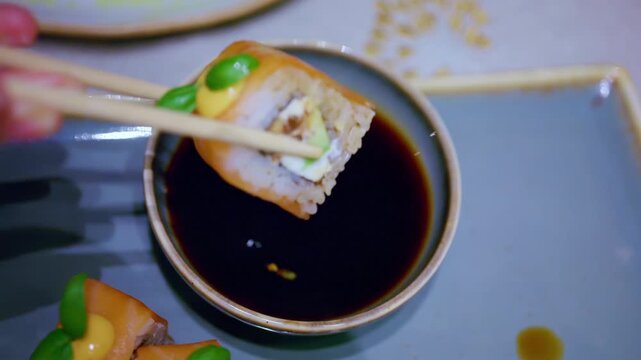 Close up pf chopsticks dipping a piece of sushi into soy sauce