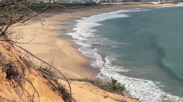 Fixed elevated view of sandy beach and gentle waves along the coastline in Barbate, Cadiz, Spain.