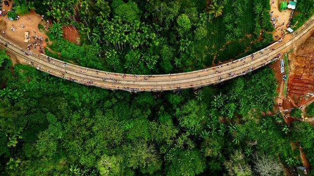 A drone shot of the Nine Arches Bridge in Sri Lanka shows the iconic curved railway viaduct spanning a lush tropical ravine. The historic stone and brick bridge arches gracefully through dense green j
