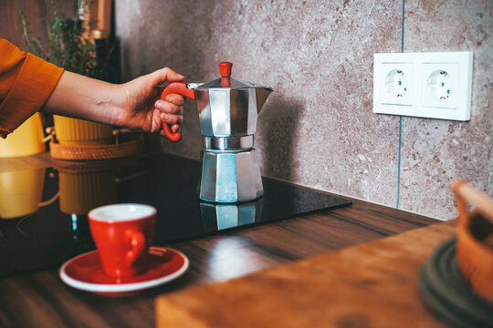 Woman hand taking silver moka pot from induction stove. Professional espresso brewing process and morning energy boost.