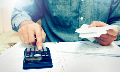 Fototapeta premium Young asian man using calculator and calculating bills to budgeting and tax calculation monthly expenses. budget management and accounting on table at home.