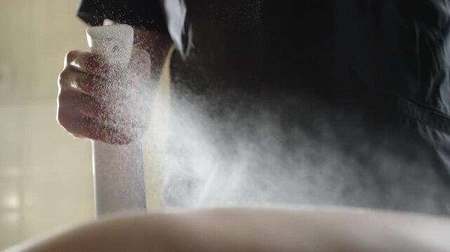 Close-up of a person using a white spray bottle to apply a fine mist over skin, capturing the aerosol cloud and trigger action during a hygiene treatment or spa application