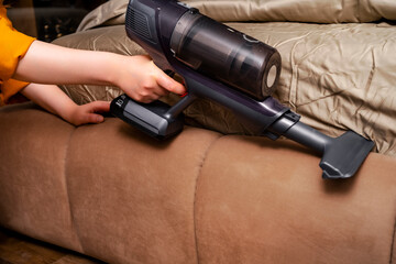 Naklejka premium Woman hand using cordless handheld vacuum cleaner for bed upholstery. Modern portable technology for fast and effective dust removal in bedroom.