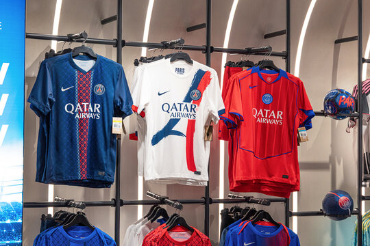 2 December 2025, Qatar, Hamad airport: Qatar Airways on Paris Saint Germain football jerseys hanging on display in a retail sportswear store