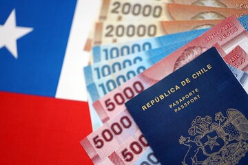 Chile Republic passport lies on flag with chilean pesos money bills close up. Chilean blue new passport book in details