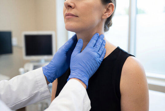 Doctor performing neck palpation during clinical exam to a female patient checking thyroid and lymph nodes in a medical office.
