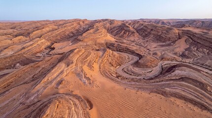 Aerial view of rugged desert landscape with winding sandy dunes and rocky formations under clear blue sky