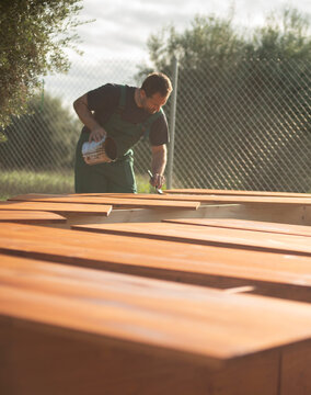 Man applying protective wood stain on planks outdoor