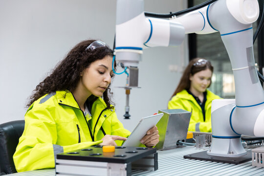 Female engineer operating collaborative robotic arm in smart factory, using tablet for quality control, automation monitoring, highlighting precision engineering, advanced manufacturing technology.
