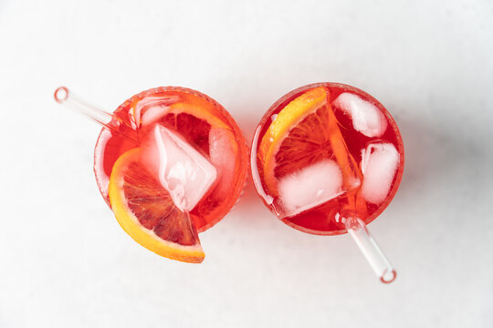 Top View Refreshing Red Orange Drink with Ice in Tall Glasses on Light Background, Fresh Summer Citrus Beverage