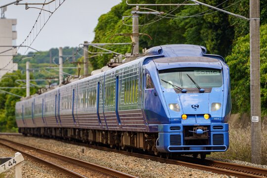 Fukuoka, Japan - 2025 June 06: A JR Kyushu 883 series "Sonic" limited express train (formation AO-4) runs on the railway track against a background of green trees. 