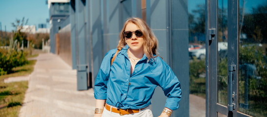 Obraz premium Confident woman in blue shirt on city background. Modern urban fashion and personality.