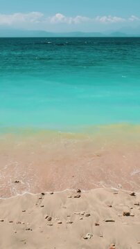 Young woman strolling along sandy beach next to the ocean, with waves gently lapping at the shore under a clear blue sky. Amazing natural summer scenery. Travel, tourism, holiday. Slow motion 4K